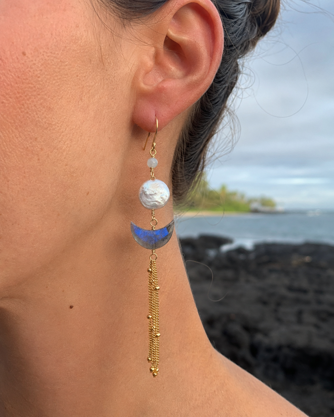 Earring with a blue and gold design worn by a person with a blurred natural background