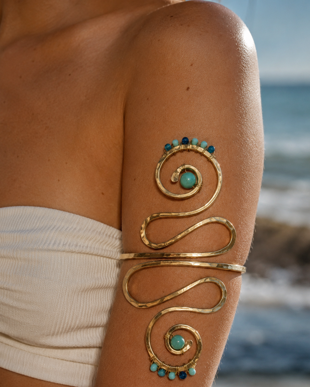 Gold arm cuff with turquoise stones on a person's arm by the ocean.